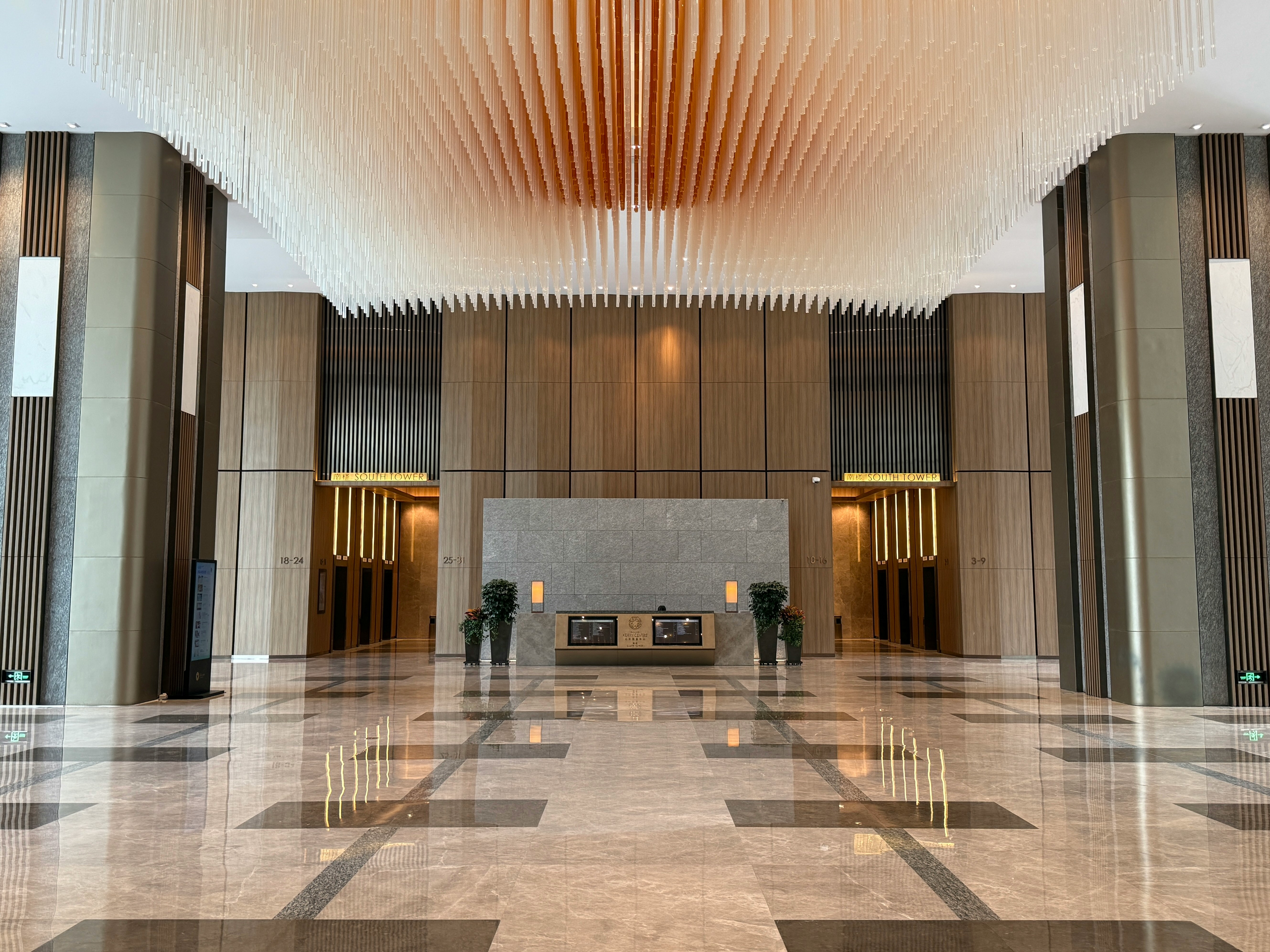 Polished marble lobby floor with a reflective geometric tile pattern, reception desk and a dramatic hanging light fixture overhead