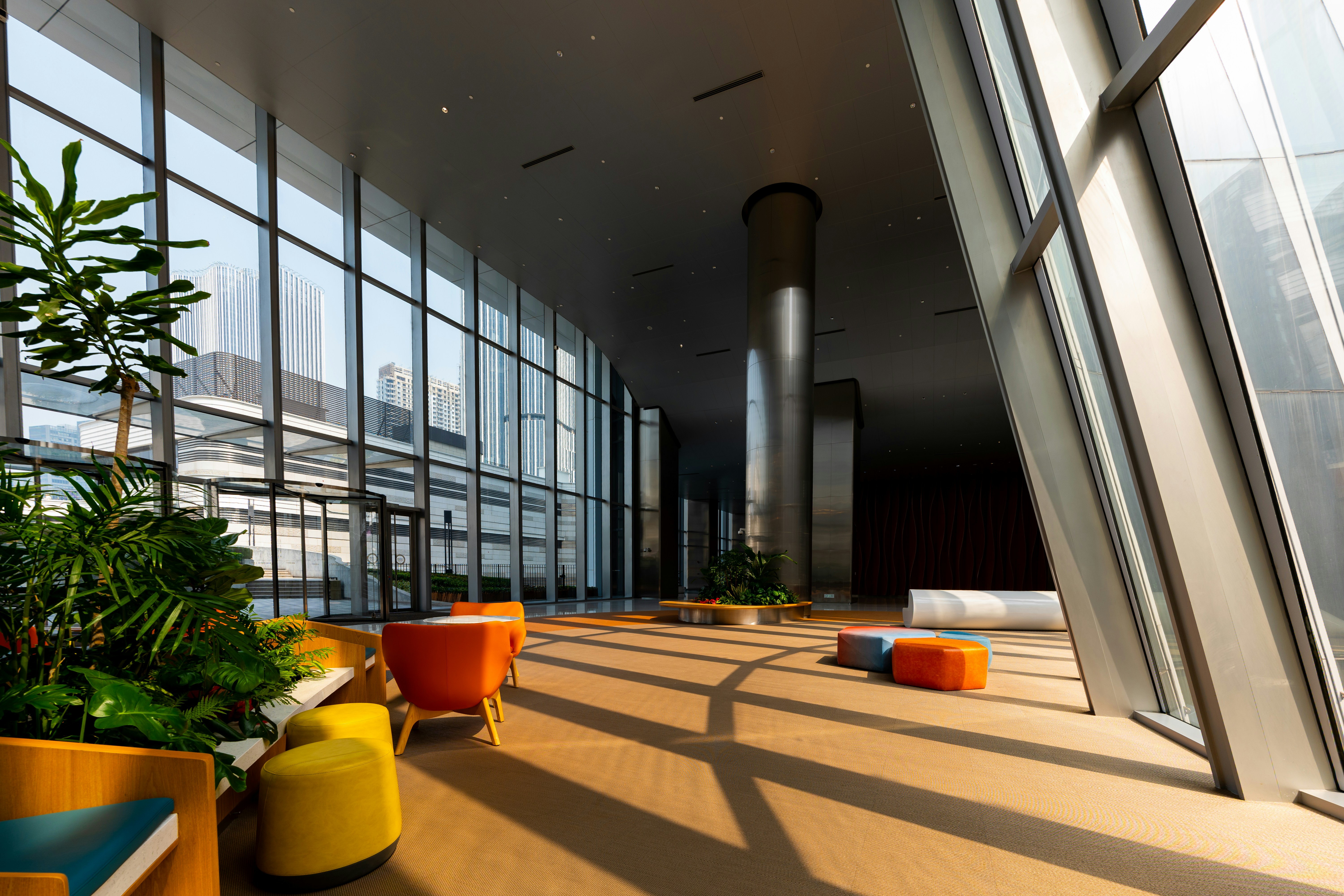 Modern office lobby with floor-to-ceiling glazing, colourful lounge seating and polished floor tile overlooking a city skyline