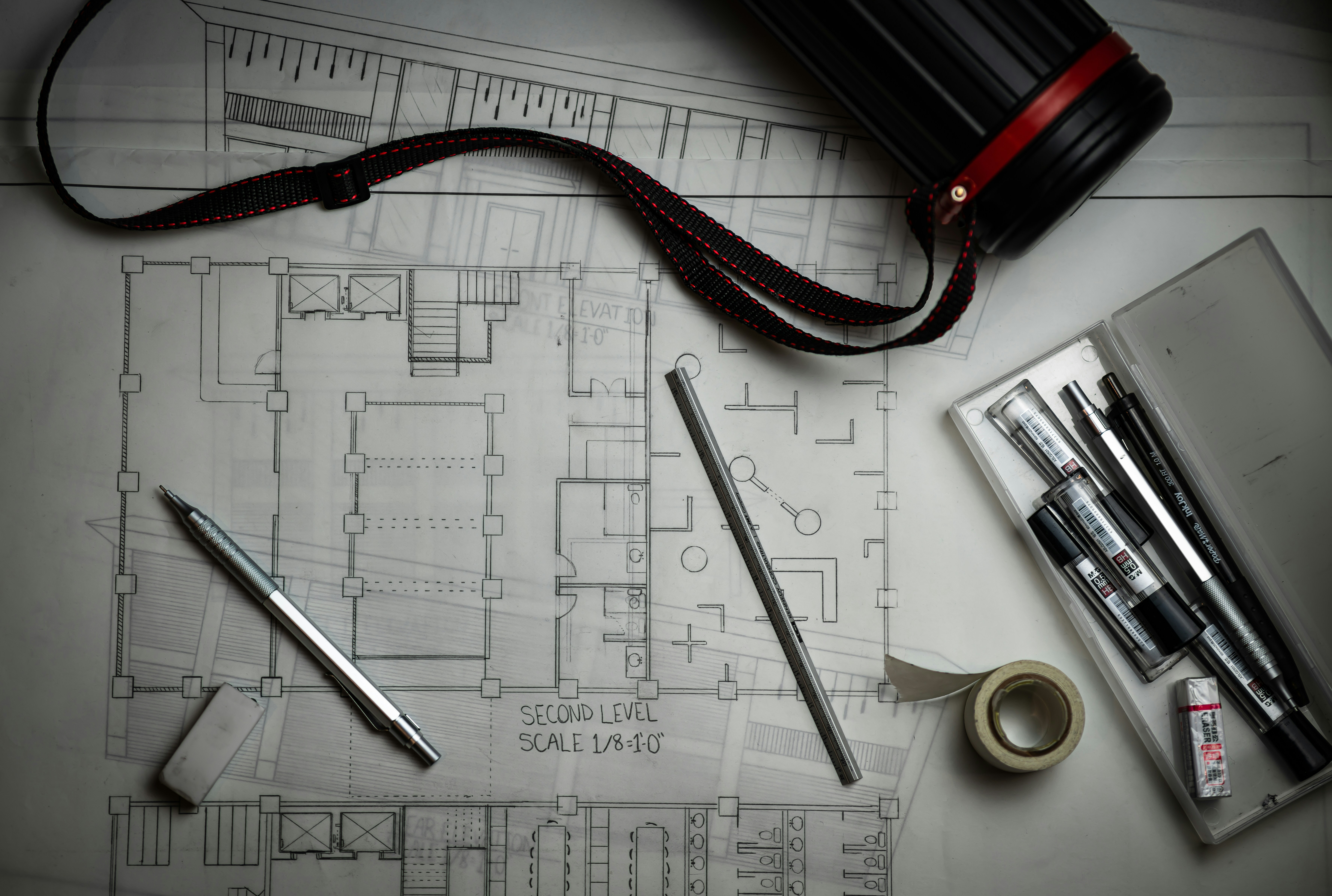 Overhead view of an architectural floor plan drawing surrounded by drafting tools — mechanical pencil, ruler, eraser and pens